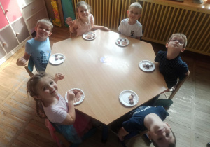 Dzieci przy stoliku spożywają zamoczone owoce w czekoladzie.