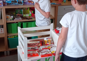 Zdjęcie przedstawia dwóch chłopców bawiących się w sklep, jeden chłopiec podaje towar a drugi kupuje