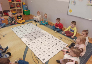 Zdjęcie przedstawiające dzieci z grupy Biedronki, siedzące przy dywaniku glottodydaktycznym.