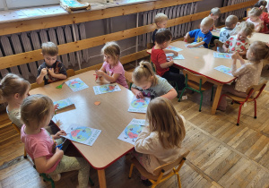 Dzieci siedzą przy stolikach, wycinają puzzle.
