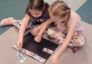 Dwie dziewczynki siedzą na dywanie i dopasowują kształty.