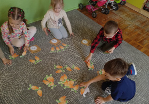 Dzieci wykonują na dywanie zadania matematyczne przy użyciu symboli marchewek