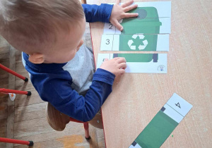 Chłopiec układa puzzle przedstawiające zielony kosz na odpady.