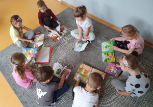 Dzieci siedzą a dywanie przeglądają wybrane przez siebie książki.