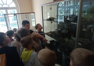 Zdjęcie przedstawia dzieci oglądających gabloty ze szczątkami samolotów w muzeum.