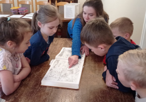 Zdjęcie przedstawia Panią Przewodnik pokazującą dzieciom historyczną książkę dotyczącą Bełchatowa.