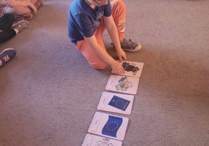 Chłopiec układa na dywanie obrazki przedstawiające symbole Unii Europejskiej