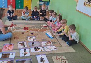 Dzieci wraz z panią siedzą na dywanie zapoznając się z nazwami, wyglądem i dźwiękami instrumentów muzycznych.