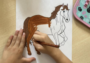 Dziewczynka koloruje rysunek konia.