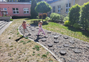 Dwie dziewczynki spacerują po ogrodzie przedszkolnym z lupami.