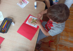Chłopiec z grupy Biedronki koloruje kartkę z życzeniami dla rodziców.
