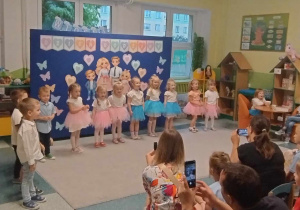 Dzieci odświętnie ubrane stoją i śpiewają piosenkę dla swoich rodziców