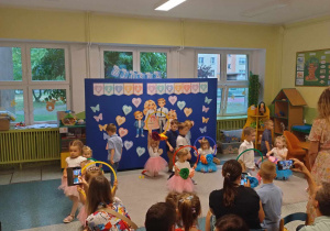 Zdjęcie przedstawia przedszkolaki, które wykonują taniec, dziewczynki w rękach trzymają obręcze z kwiatkami