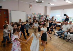 Dzieci śpiewają piosenkę i tańczą w kółeczku.
