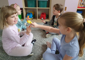 Dzieci siedzą na dywanie wykonują ćwiczenia dźwiękonaśladowcze z pacynkami zwierząt założonymi na palec