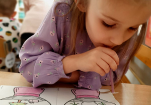 Dziewczynka wykonuje ćwiczenia oddechowe przenosząc gwiazdy na papierową kule za pomocą słomki.