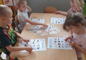 Dzieci siedzą przy stoliku, grają w logopedyczne bingo.