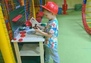 Chłopiec w czerwonym kasku bawi się zestawem małego majsterkowicza.