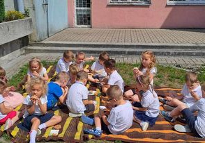 Dzieci siedzą na kocykach i zajadają smakołyki.