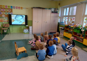 Dzieci z grupy Motylki oglądają bajkę „Poznajcie Kropkę czyli Vashti i jej historia” na tablicy multimedialnej.