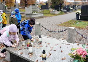 3.Dziewczynka z chłopcem stawiają znicze na płycie grobowca.