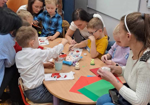 Dzieci wspólnie siedzą z rodzicami przy stoliku i malują farbami.