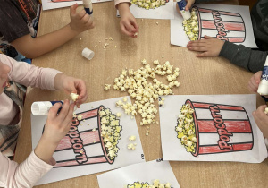 Dzieci przyklejają popcorn na pracę plastyczną.