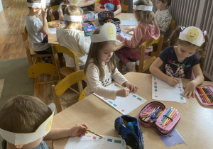 Przedszkolaki siedzą przy stolikach i wykonują kartę pracy – łączą w pary klocki.