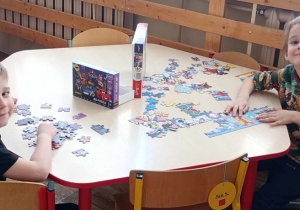 Dwaj chłopcy siedzą przy stoliku i układają puzzle.