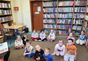 Dzieci siedzą na dywanie, pani bibliotekarka czyta książkę.