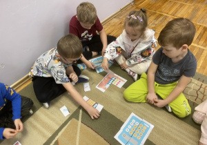 Dzieci siedzą na dywanie i układają puzzle.