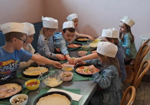 Dzieci nakładają dodatki na pizzę.