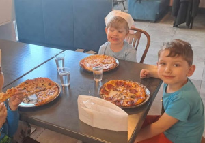 Dzieci zajadają pizzę przygotowaną przez siebie.