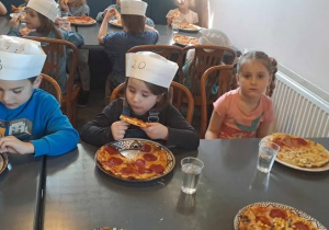 Dzieci zajadają pizzę przygotowaną przez siebie.