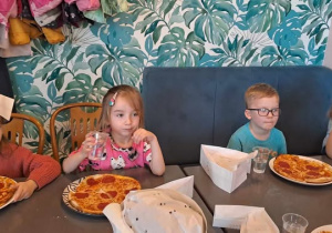 Dzieci zajadają pizzę przygotowaną przez siebie.