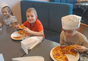 Dzieci zajadają pizzę przygotowaną przez siebie.