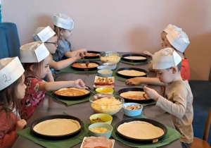 Dzieci smarują ciasto na pizzę sosem pomidorowym.