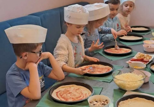 Dzieci smarują ciasto na pizzę sosem.