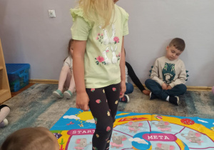 Dziewczynka z grupy „Słoneczka” stoi na macie do zabaw ruchowych.