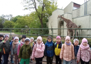 Dzieci pozują do zdjęcia, w tle dwie żyrafy.
