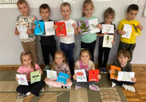 Dzieci z grupy Misie prezentują odpowiednio przyporządkowane kartki z zielnika z obrazkami, które pomalowały.