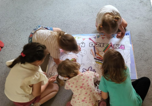 Dzieci grupowo kolorują rysunek z napisem Dzień Dziecka.
