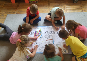 Dzieci grupowo kolorują rysunek z napisem Dzień Dziecka.