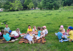 Dzieci siedzą na kocach, częstują się smakołykami.