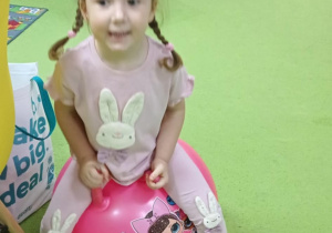 Zdjęcie przedstawia dziewczynkę skaczącą na dużej piłce.
