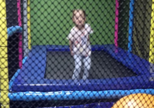 Zdjęcie przedstawia dziewczynkę skaczącą na trampolinie.
