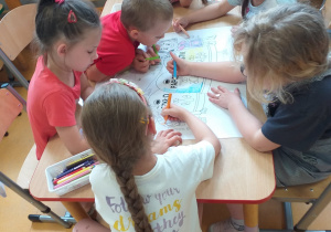 Zdjęcie przedstawia dzieci wspólnie kolorujące wielką kolorowankę.