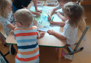 Zdjęcie przedstawia dzieci wspólnie kolorujące wielką kolorowankę.