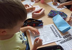 Chłopiec z grupy Słoneczka wykonuje pracę plastyczną na temat bezpiecznych wakacji.