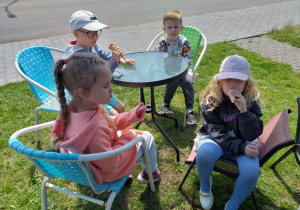 Dzieci zajadają lody przy siedząc przy stoliczkach.